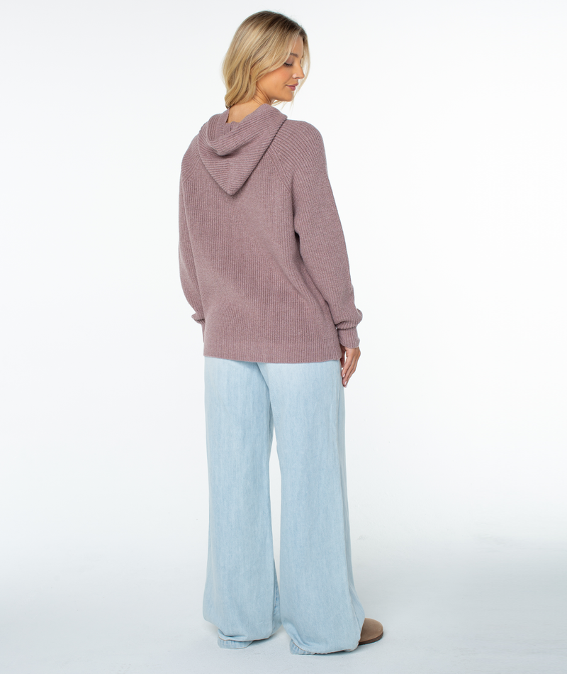 A person viewed from behind, wearing a dusty pink Roxy Cozy Town Sweater and light-wash wide-leg jeans as a winter staple.