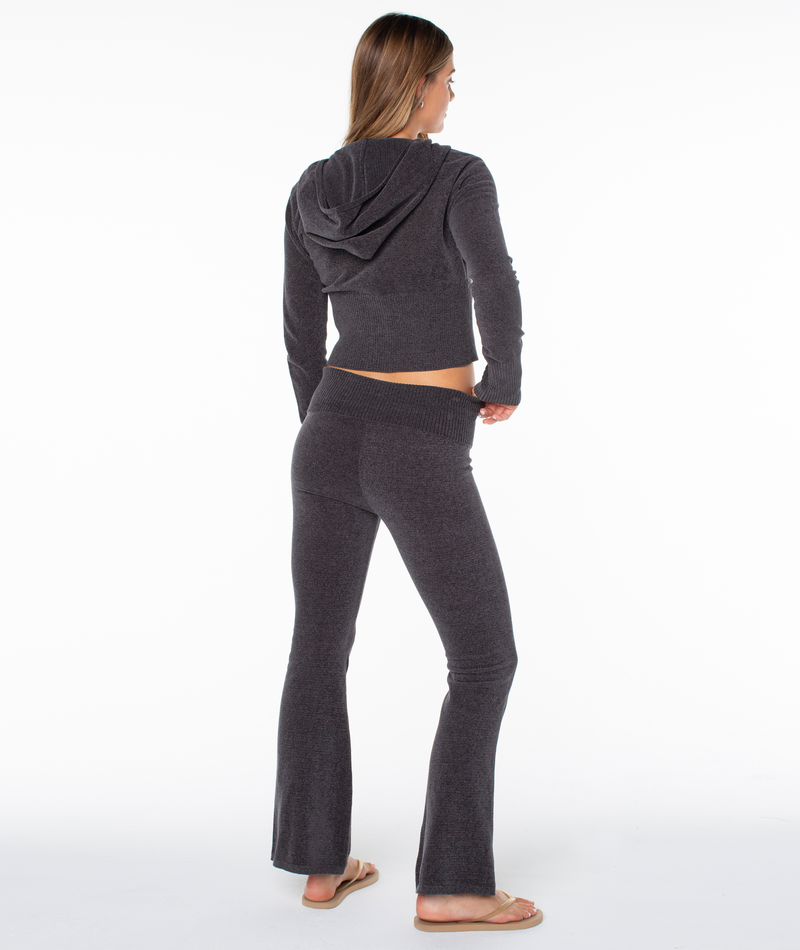 A woman wears a charcoal gray Roxy Double Daze 2 Top, a cozy hooded zip-up sweater, with matching flared pants for a comfortable fit.