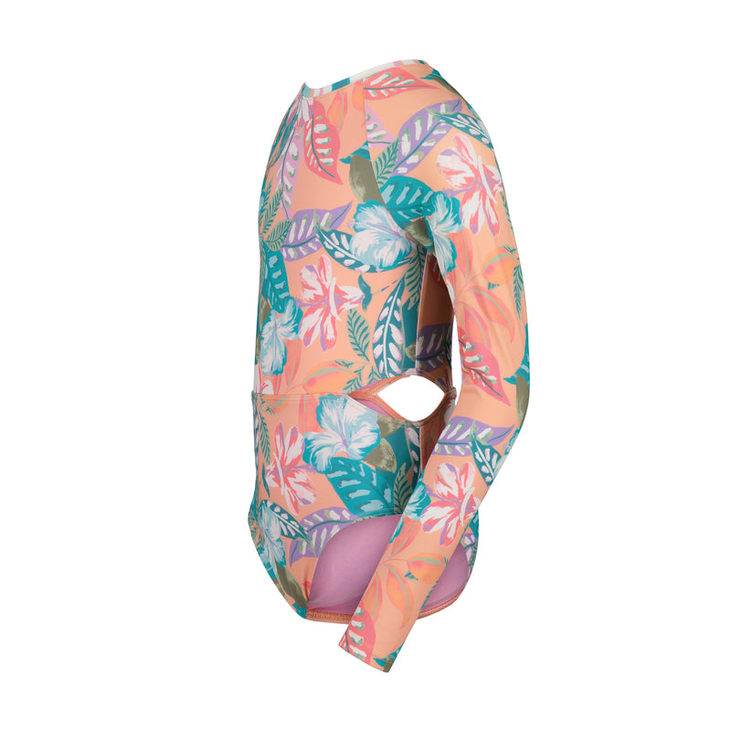 The Roxy Girls' Hot Tropics Onesie is a long sleeve, one-piece swimsuit with a peach background, tropical green, white, and pink floral print, plus a trendy side cut-out—perfect for sunny days by the water.