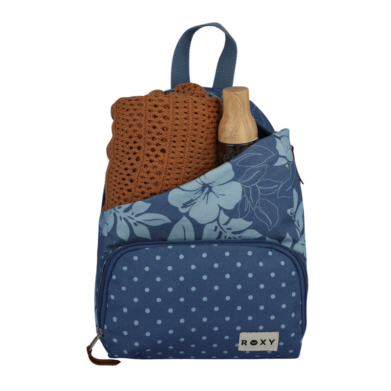 A blue Roxy Always Core Canvas Backpack with floral and polka dot patterns, holding a folded brown knit sweater and a wooden water bottle in the front pocket.