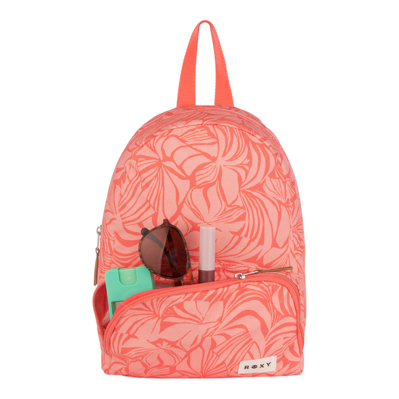 A pink, floral-patterned ROXY Always Core Canvas Backpack with a small front pocket that holds sunglasses, green hand sanitizer, and a pink lipstick. This compact backpack showcases an eco-conscious design with a red handle and the signature ROXY label at the bottom.