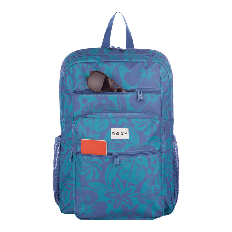 The Roxy Campus Crush Backpack features a blue and teal floral design in recycled polyester, with a front pocket holding an orange notebook and a top pocket containing sunglasses. This backpack is equipped with convenient organizer pockets, side mesh pockets, a padded laptop sleeve, and displays the ROXY label on the front.