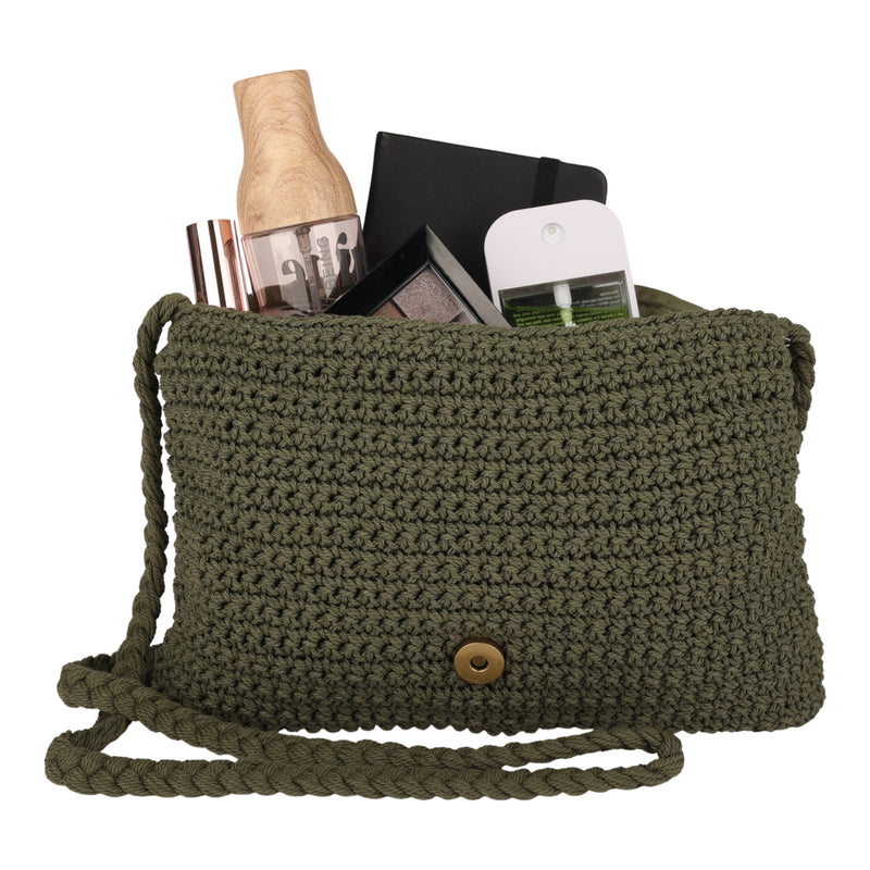 The Roxy Chips And Guac Medium Crossbody Bag in green crochet is open, showcasing everyday essentials inside, such as makeup, a notebook, a phone, and a wooden bottle.