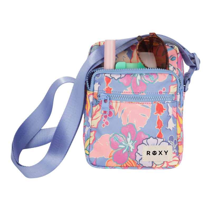 A compact ROXY Current Mood Crossbody Bag featuring a floral pattern and a light blue adjustable strap, with sunglasses, a pink item, and a green item stored in the front pocket.