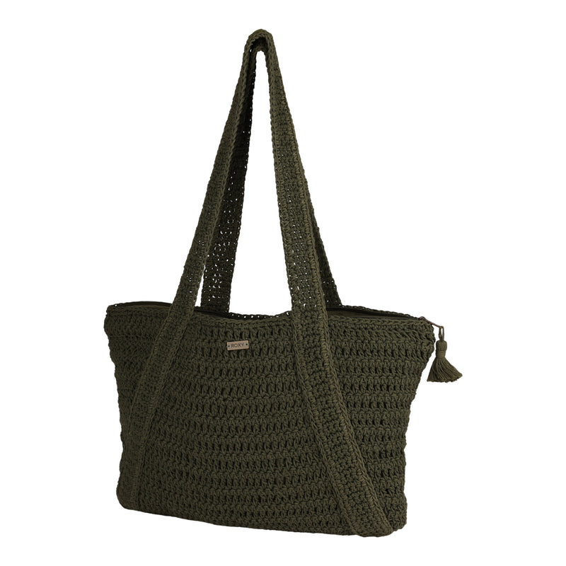The Roxy Chips And Guac Tote Bag is a dark green crocheted tote featuring double handles, a zippered top closure with a small tassel attached, and a small rectangular metal logo plate on the front. Set against a plain white background, this spacious bag is the perfect travel companion for your everyday adventures.