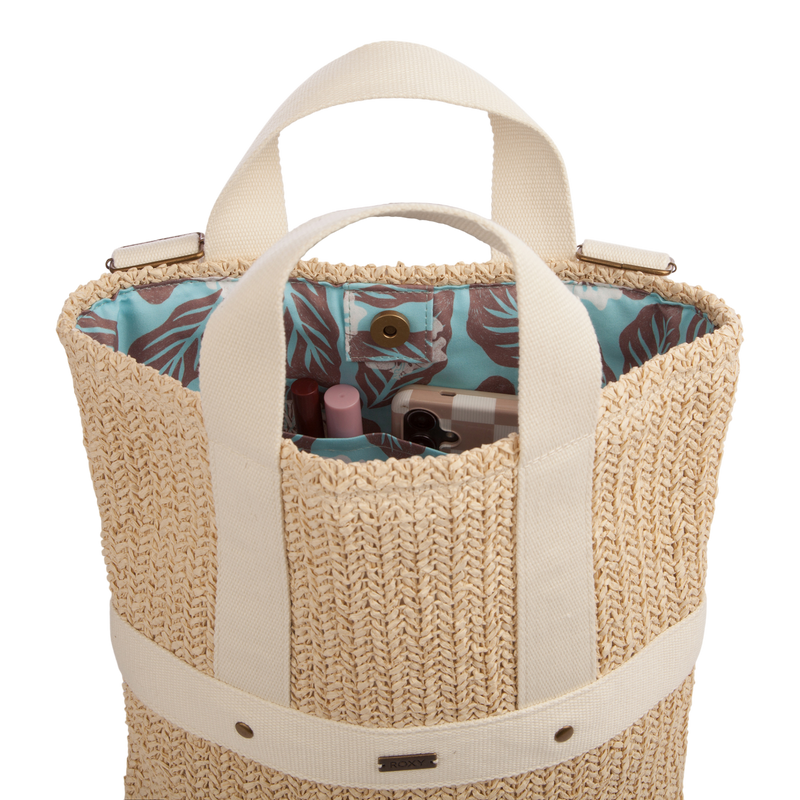 The Sunny Stash Backpack by Roxy features woven straw construction with cream handles and opens to reveal a blue patterned lining and multiple cosmetic items inside—delivering the perfect balance of charm and functionality for anyone looking for a stylish or versatile beach backpack.