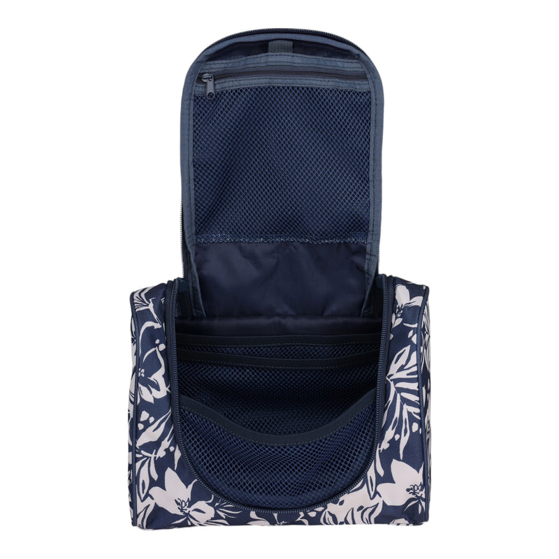 The Roxy Travel Dance Toiletry Kit is shown open in navy blue with white floral patterns. Crafted from recycled polyester, it features mesh pockets and zippered compartments inside for organized travel storage.
