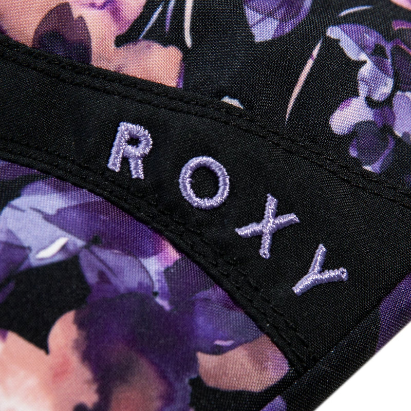 Close-up of fabric from the Roxy Girls Jetty Mitts by Roxy, showing the word ROXY stitched in light purple thread on a black background with a purple and pink floral pattern.