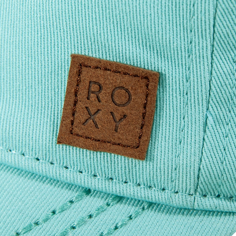 Close-up of the Roxy Extra Innings Baseball Cap for women, made from light blue cotton twill, featuring a curved visor and a brown square patch on the front with “ROXY” in capital letters.