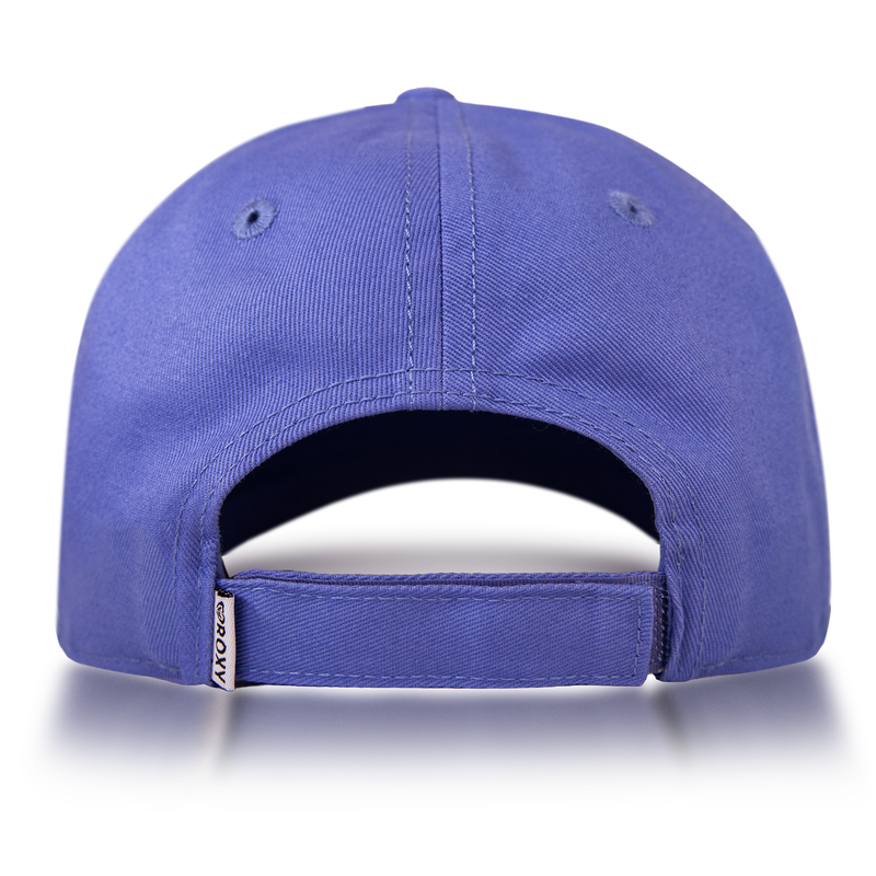 The Roxy Next Level Cap is a blue women’s baseball hat crafted from soft cotton twill. Viewed from the back, it features an adjustable strap, two stitched eyelets, and a small fabric tag with text attached to the left side of the strap opening.