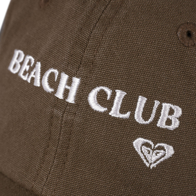 Close-up of brown fabric on the Roxy Toadstool Cap, featuring BEACH CLUB embroidered in white thread and a small heart-shaped logo below the text, reflecting the cool style often seen on sleek baseball hats.