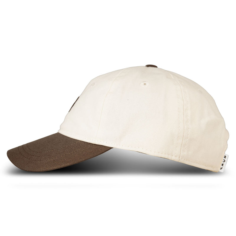 A side view of the Roxy Next Level Cap, a women’s baseball hat made from soft cotton twill with a cream-colored crown and a brown curved visor, set against a white background.