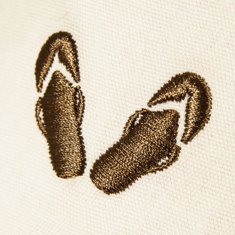 Cream-colored cotton twill Next Level Cap by Roxy, featuring brown embroidery of a pair of flip-flops with detailed stitching on both the soles and straps.
