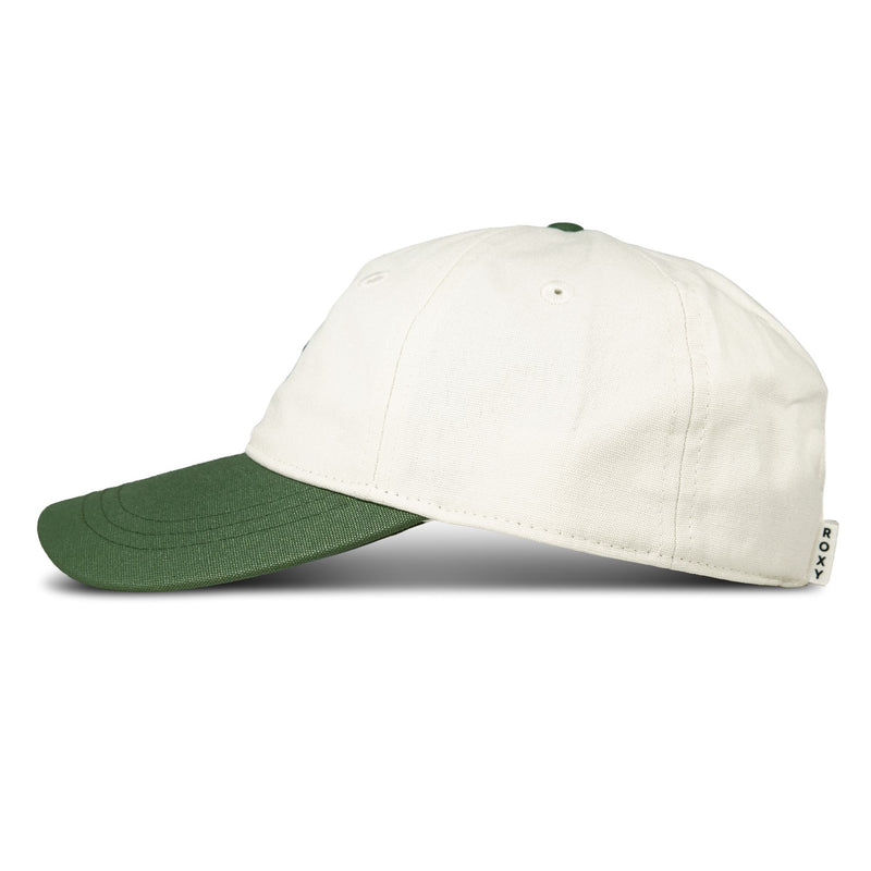 A side view of the Next Level Cap by Roxy, a women’s white baseball hat with a green curved visor. Made from soft cotton twill, it features a small fabric tag with the ROXY brand name on the back. The cap is displayed on a white background with a shadow underneath.