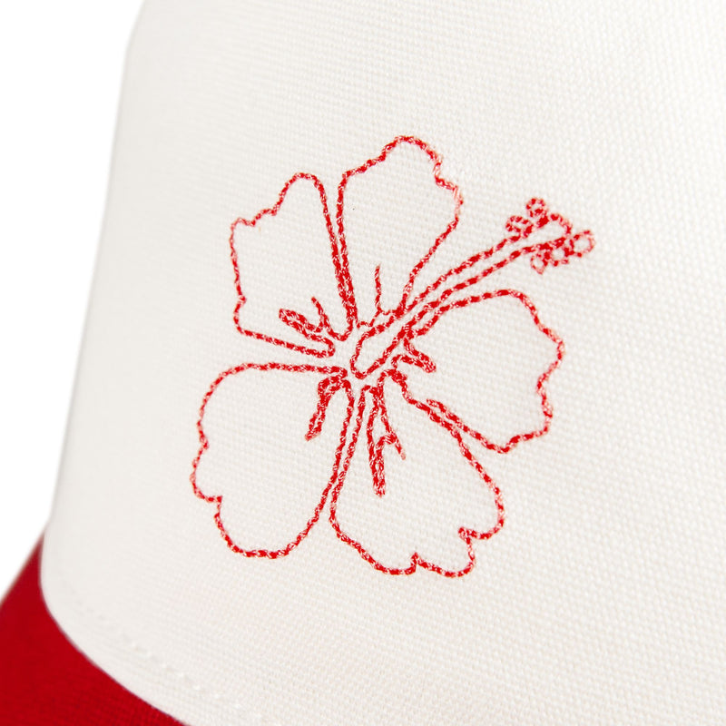 Close-up of white cotton twill fabric on the Roxy Next Level Cap, featuring a red-stitched outline of a hibiscus flower, reminiscent of designs often seen on women’s baseball hats with curved visors. The edge of a red section is visible at the bottom left.