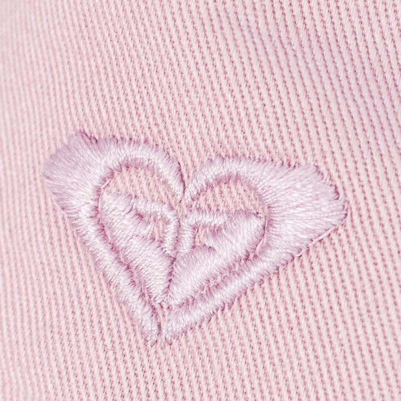 Closeup of a light pink embroidered heart on pink ribbed fabric—this detailed threadwork and rich texture make the Roxy TW Dear Believer Baseball Cap a perfect everyday accessory to complement your casual outfits.