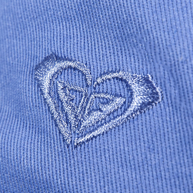 Close-up of the TW Dear Believer Baseball Cap by Roxy, featuring a blue fabric with a heart-shaped logo elegantly embroidered in shiny blue thread. The raised stitching stands out against the textured background, adding a charming touch to this versatile everyday accessory.