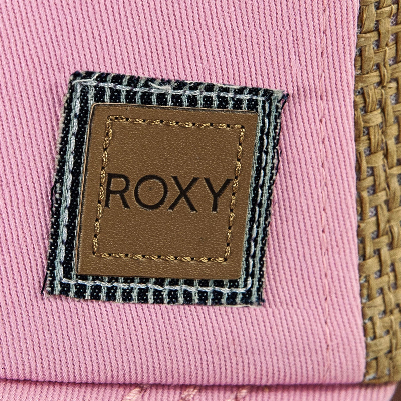A brown leather patch featuring the word “ROXY” stitched onto pink fabric with a black-and-white striped border, set beside a woven straw section, showcases the chic details of the Roxy Incognito Cap—a stylish women’s cap designed for fashionable comfort.