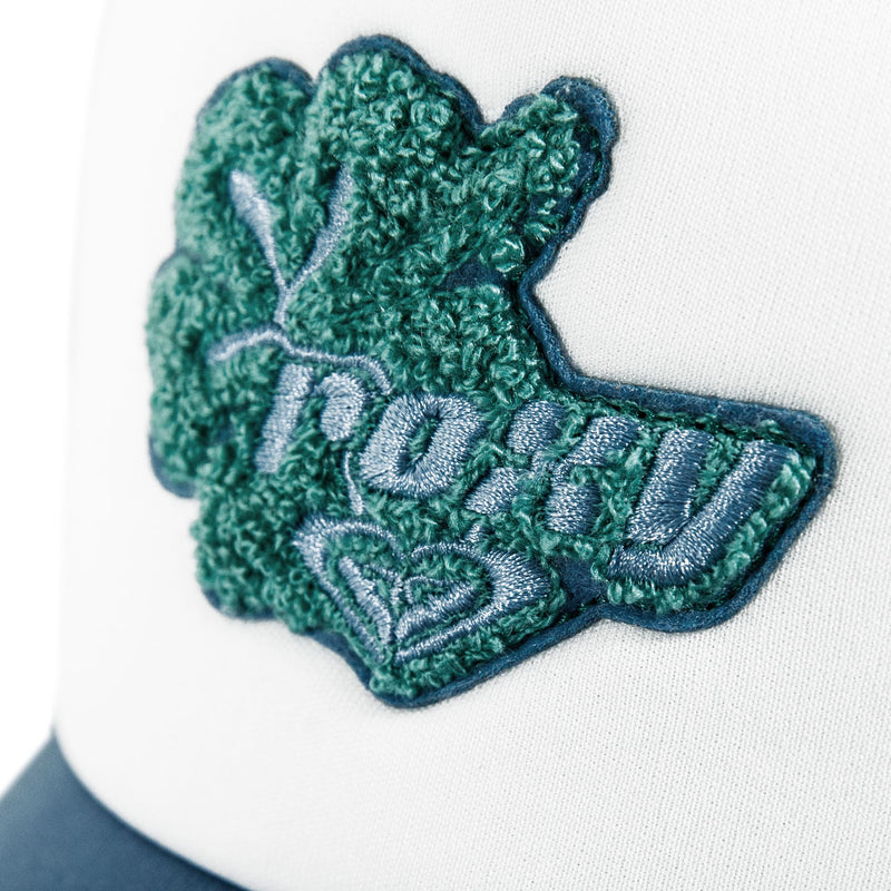 Close-up of a green textured clover-shaped patch with “POPFV” and a blue heart embroidered on white fabric, likely from the Roxy Island Ride Trucker hat.