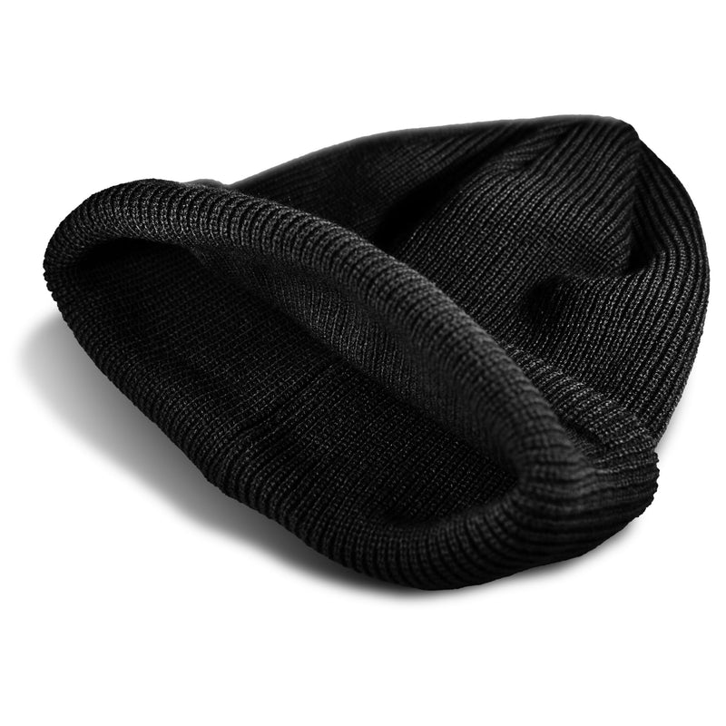 The Roxy Blizzard Beanie, a black ribbed chunky knit hat, lies flat and partially folded on a white surface, casting a subtle shadow.