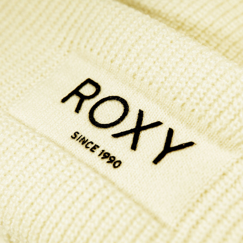 Close-up of a cream-colored chunky knit beanie featuring a white label with “Roxy Since 1990” in black text. The visible knit texture emphasizes the cozy design of the Roxy Blizzard Beanie for women.