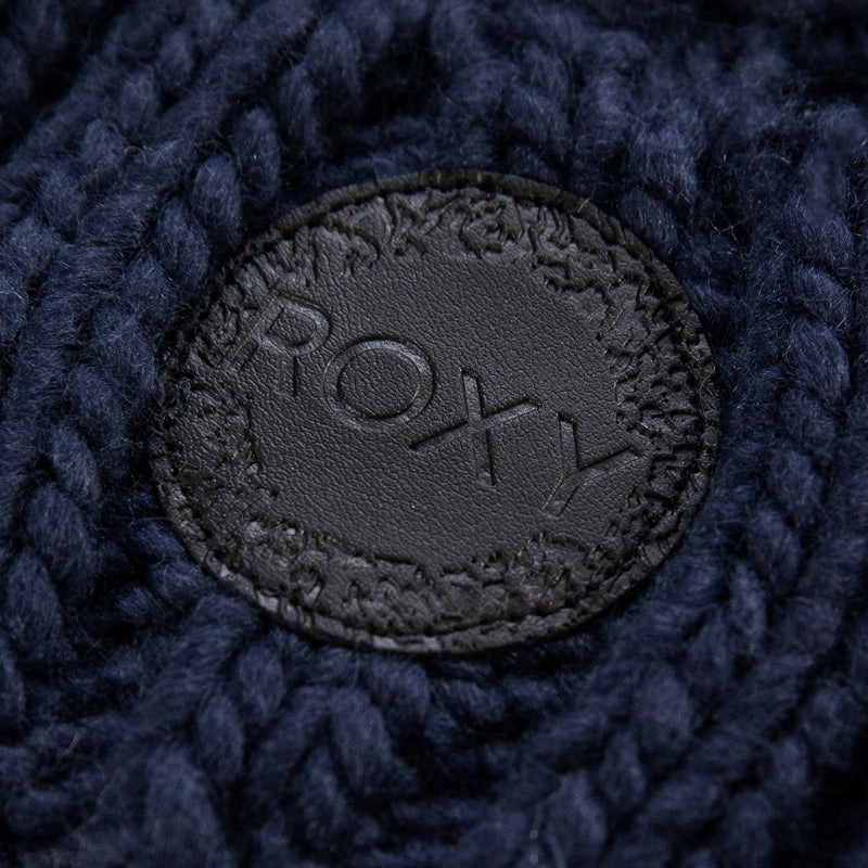 A close-up of a black leather patch embossed with “Roxy” and sewn onto the dark blue cable knit fabric of the Tram Beanie. This women’s beanie from Roxy features a cozy fleece-lined interior for extra warmth.