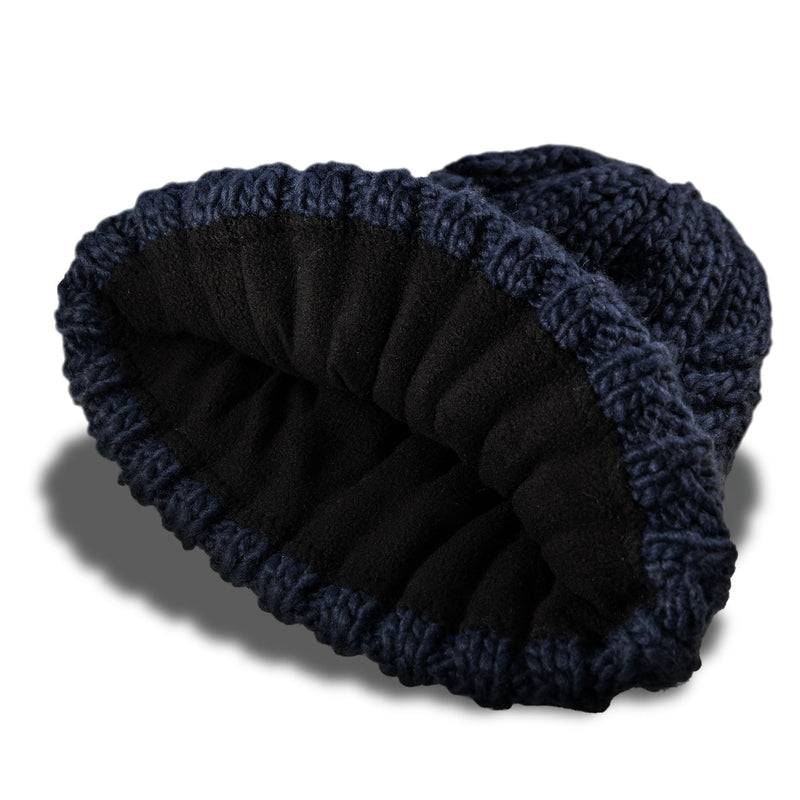 The Roxy Tram Beanie is a navy blue cable knit hat for women, featuring a black fleece-lined interior, showcased on a white background with a soft shadow beneath.
