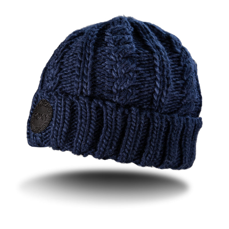 A navy blue Roxy Tram Beanie with a ribbed cable knit pattern and a folded brim, featuring a round black patch on the side. Designed for women and fleece lined for extra warmth, the beanie casts a shadow on a white background.
