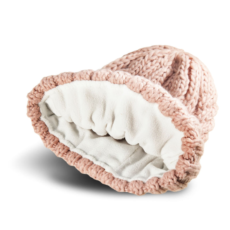 The Roxy Tram Beanie, a pink cable knit hat with a soft white fleece lining, is shown lying on its side against a white background.