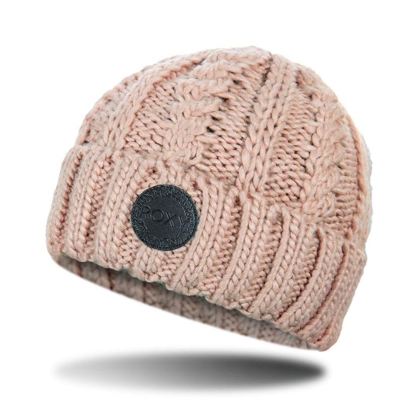 The Roxy Tram Beanie is a cozy pink cable knit hat featuring a folded brim and a round black patch on the front. Displayed against a white background with a soft shadow beneath, this stylish women’s beanie effortlessly adds warmth and flair to any winter outfit.