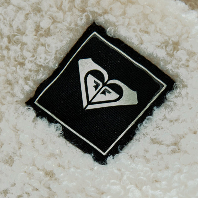 A black diamond-shaped patch with a white heart-shaped logo stitched onto a textured cream-colored Roxy Valwood Beanie.
