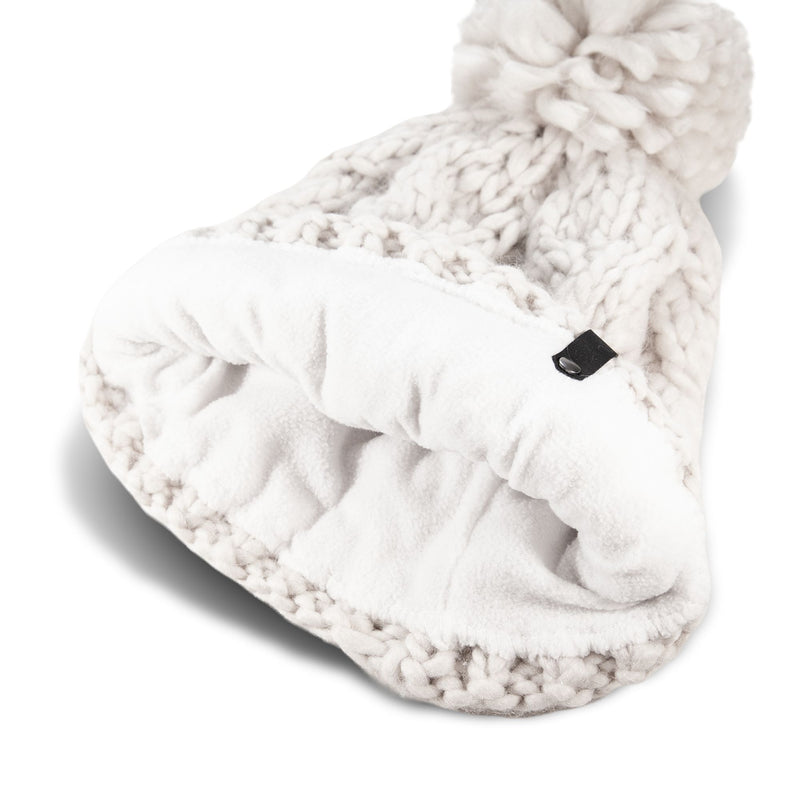 The Roxy Winter Beanie, a chunky white knit women’s hat with a large pom-pom and soft white fleece lining, is shown lying on its side with the interior visible.