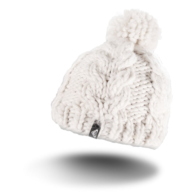 The Roxy Winter Beanie is a cream-colored, chunky knit hat with a large pom-pom on top, accented by a small black triangular tag on the brim and lined with cozy fleece for extra warmth. It is displayed against a white background with a subtle shadow underneath.