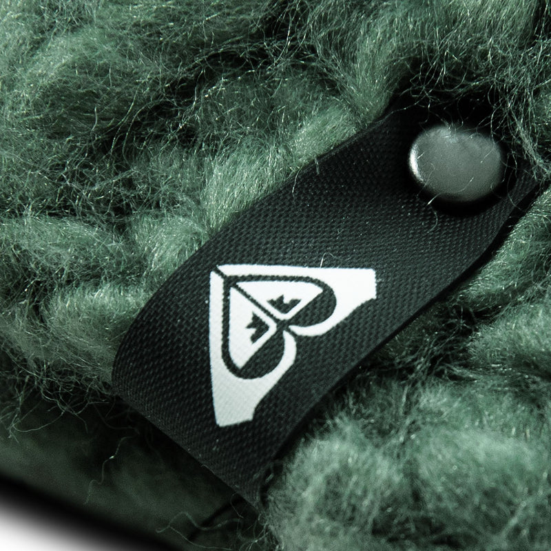 A close-up of a black Roxy tag with a white heart-shaped logo sewn onto chunky knit, textured green fabric—perfectly capturing the cozy detail of the Winter Beanie.