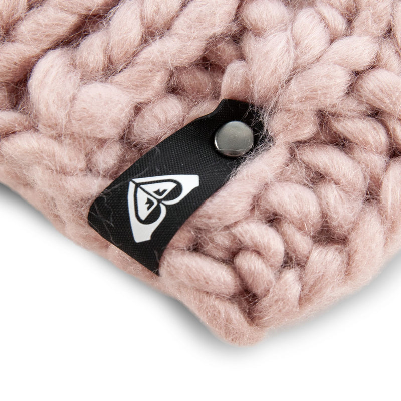 Close-up of a pink chunky knit fabric from the Roxy Winter Beanie, perfect for cozy winter days, featuring a black and white fabric tag with a heart-shaped logo and a metal button.
