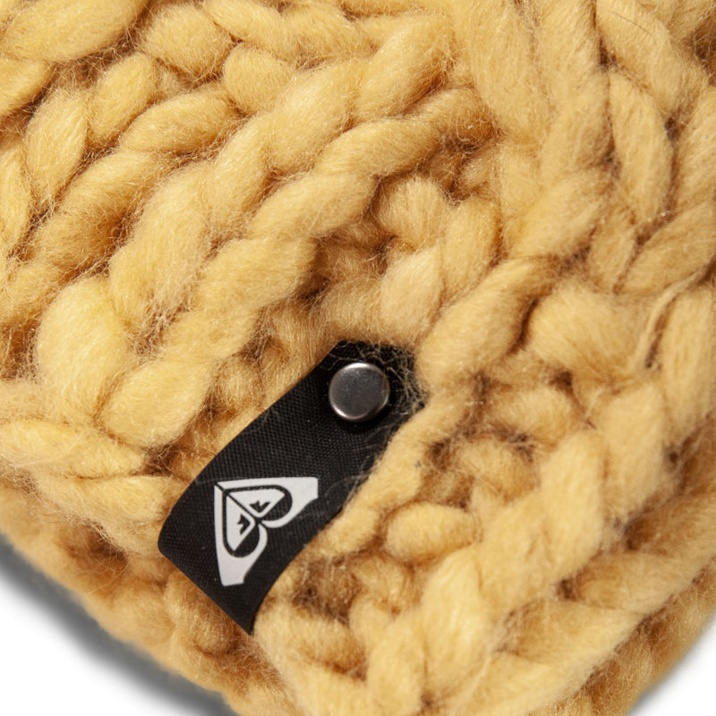 Close-up of thick, yellow chunky knit fabric with a black Roxy tag featuring a white logo and a metal button attached to the stitches—perfect detailing on this cozy women’s Winter Beanie.