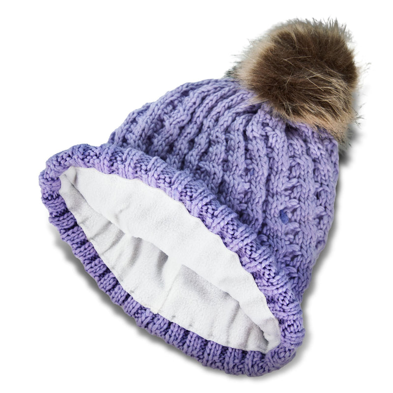 The Roxy Girls Blizzard Girl Beanie by Roxy is a purple cable knit hat featuring a fluffy faux fur pom on top and a soft polar fleece lining, displayed on a white background.