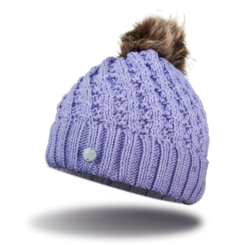 The Roxy Girls Blizzard Girl Beanie is a lavender cable knit hat with a ribbed cuff, featuring a faux fur pom on top and a small round metal tag on the front.