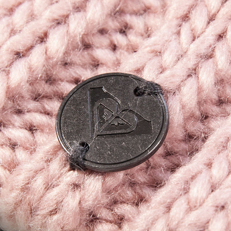 A close-up of a round, black button with a raised Roxy logo, sewn onto the chunky, soft, light pink cable knit fabric of the Roxy Girls Blizzard Girl Beanie.