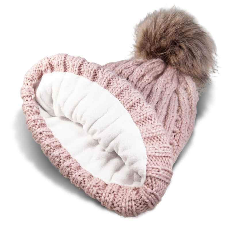 The Roxy Girls Blizzard Girl Beanie by Roxy is a pink cable knit beanie featuring a fluffy brown faux fur pom on top, shown inside out to display its cozy polar fleece lining.