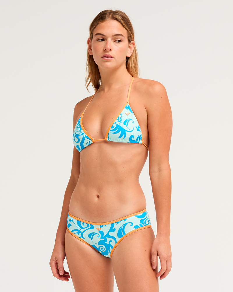 A woman with a neutral expression stands against a plain background wearing the Roxy Kauai Bikini Top, featuring a blue and white tropical print with orange trim.