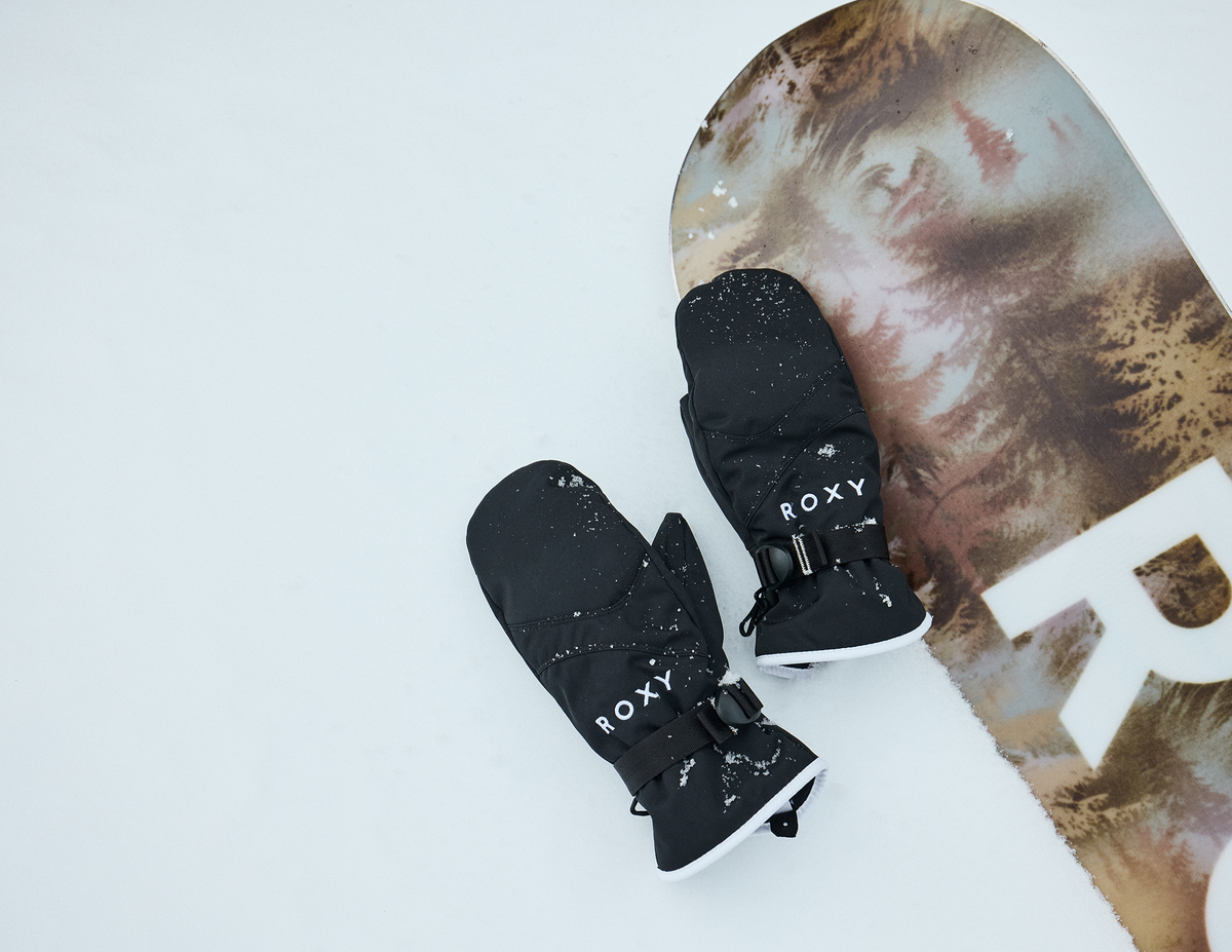 Black Roxy snow mittens resting on a snowboard in the snow.
