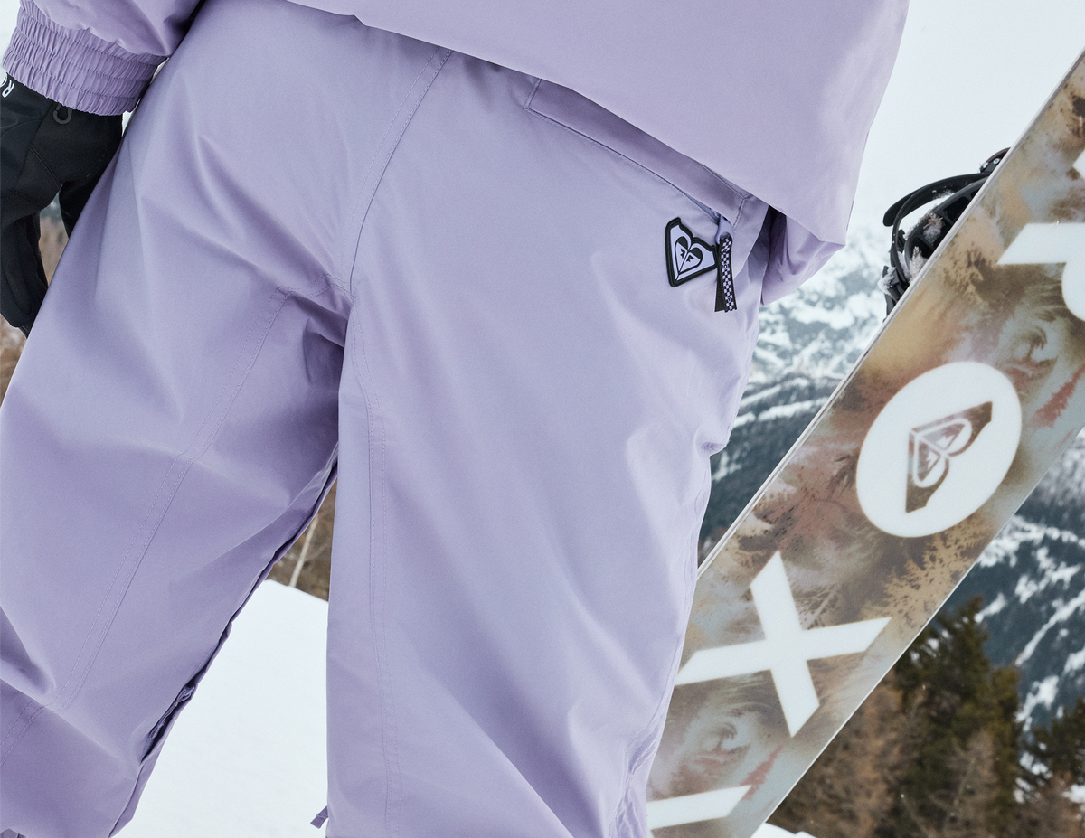 Close-up of lavender Roxy snow pants beside a snowboard.