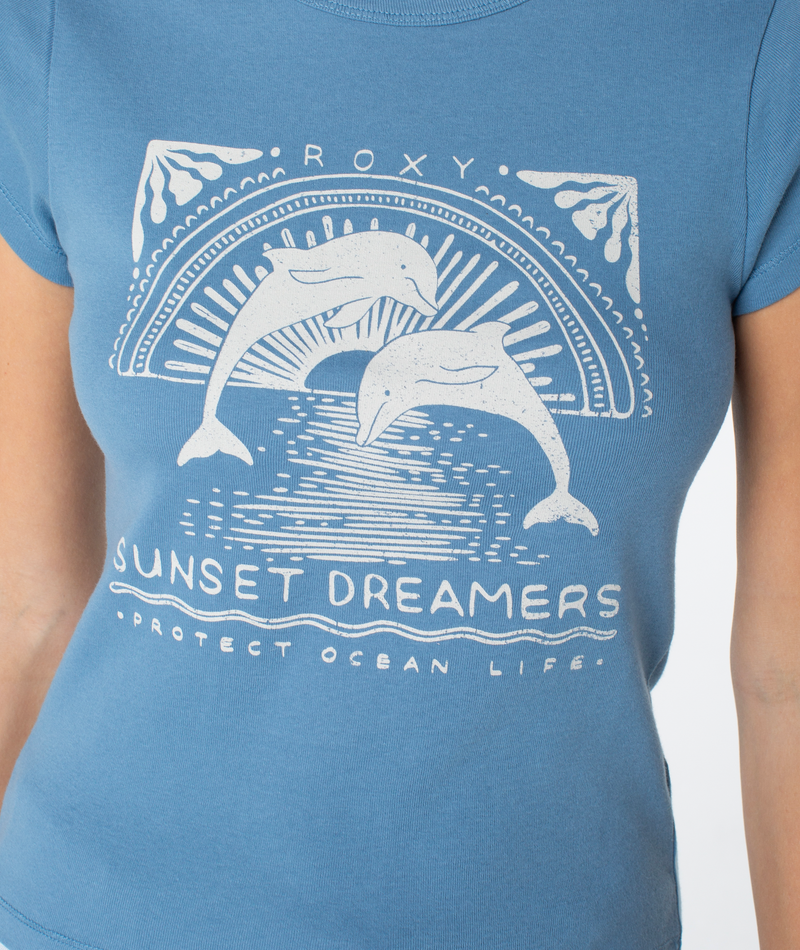 Blue Sunset Dreams 90S Baby Tee with a white graphic of two dolphins jumping in front of a sun, featuring the text ROXY, SUNSET DREAMERS, and PROTECT OCEAN LIFE.