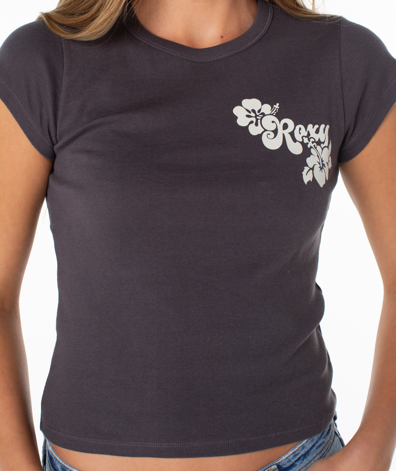Woman wearing a fitted, short-sleeve Hibiscus View 90S Baby Tee by Roxy in Phantom Hibiscus View, featuring a white logo and floral design on the chest, standing against a white background.