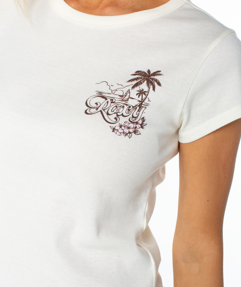 A person wears a white Roxy Kinda Salty 90S Baby Tee featuring palm trees and flowers on the chest. Only their upper torso and part of one arm are visible.