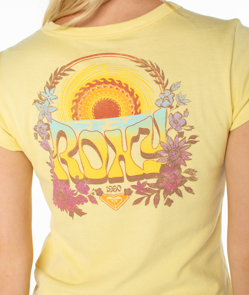 A person in the Roxy Tribal Sunset 90S Baby Tee featuring a yellow, retro design with a colorful back graphic of a sunrise, flowers, bold ROXY lettering, and “1990” for beachy vibes.