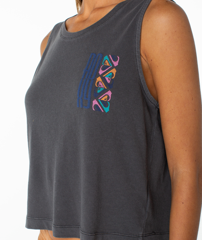 A person wearing the Roxy Oceanview Wildflower Tank—a sleeveless, dark gray crop top featuring colorful geometric embroidery on the left chest. The upper body is shown against a white background, highlighting an effortless tomboy style.