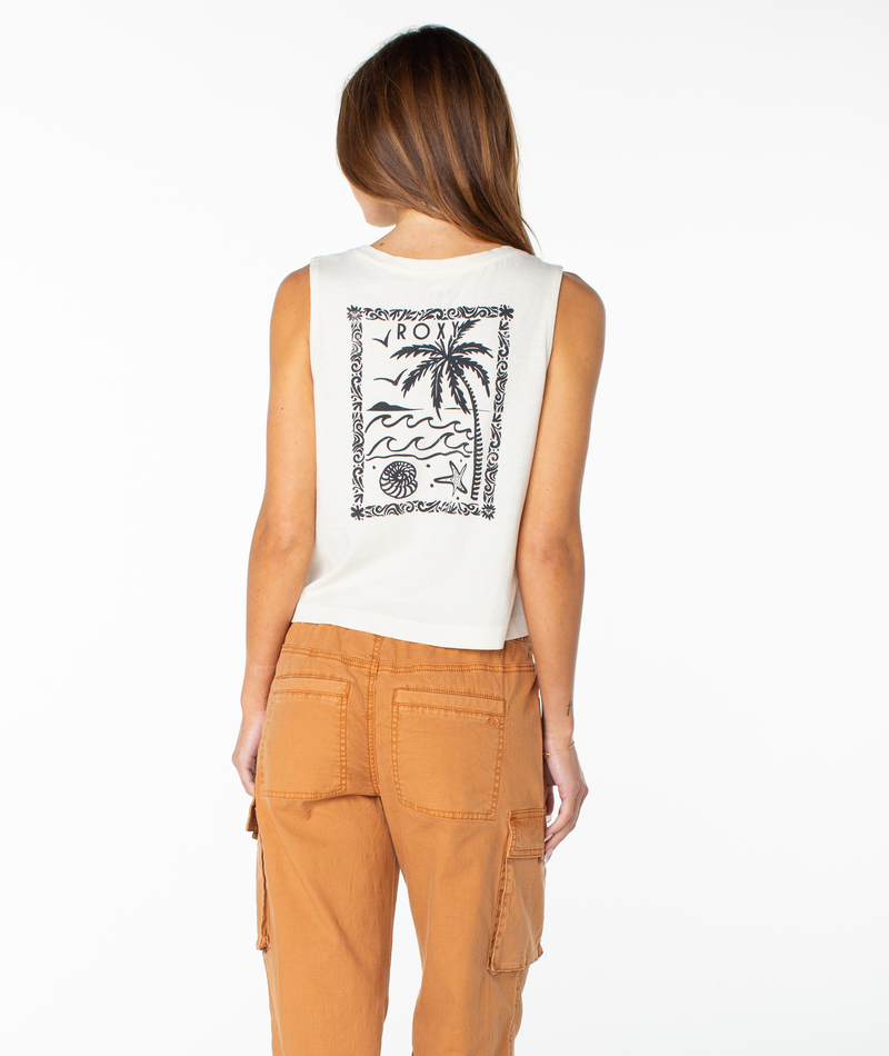 A woman with long brown hair faces away, wearing the sleeveless white Roxy Palm Poster Wildflower Tank featuring a black tropical graphic, paired with light brown cargo pants for an effortlessly beachy chic look.