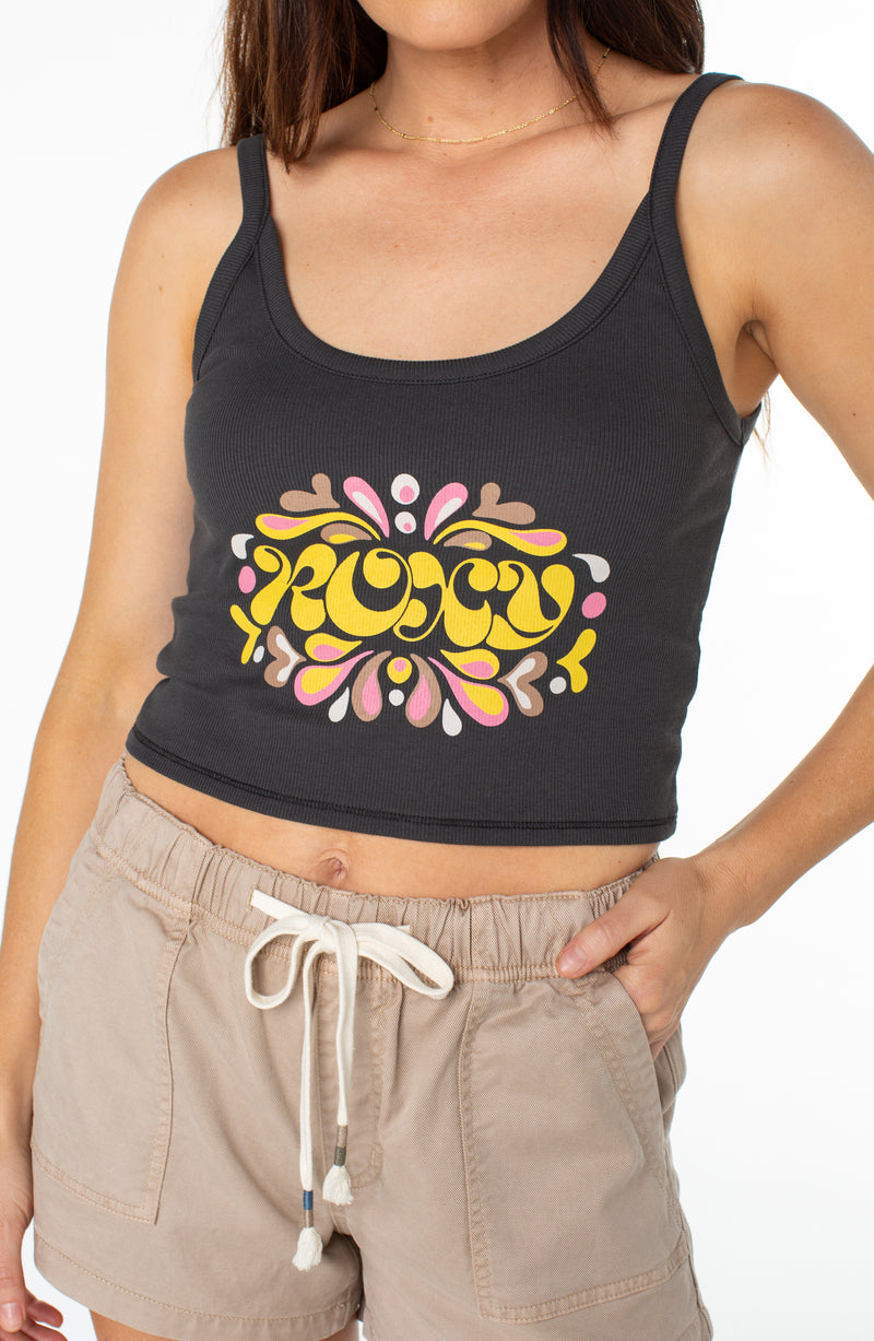 A person wearing a black Roxy Epic Vibe Wanderer Tank featuring a yellow and pink floral graphic print and khaki drawstring shorts.